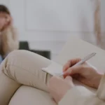 Therapist writing notes during a forensic psychology session with a distressed patient.