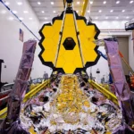 The James Webb Space Telescope floating in deep space, with its golden hexagonal mirrors reflecting cosmic light.